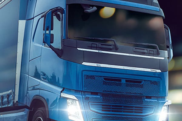 Camion Volvo bleu phares allumés la nuit Gros plan sur l'avant d'un camion Volvo bleu vif circulant de nuit, ses phares à LED éclairant la route.